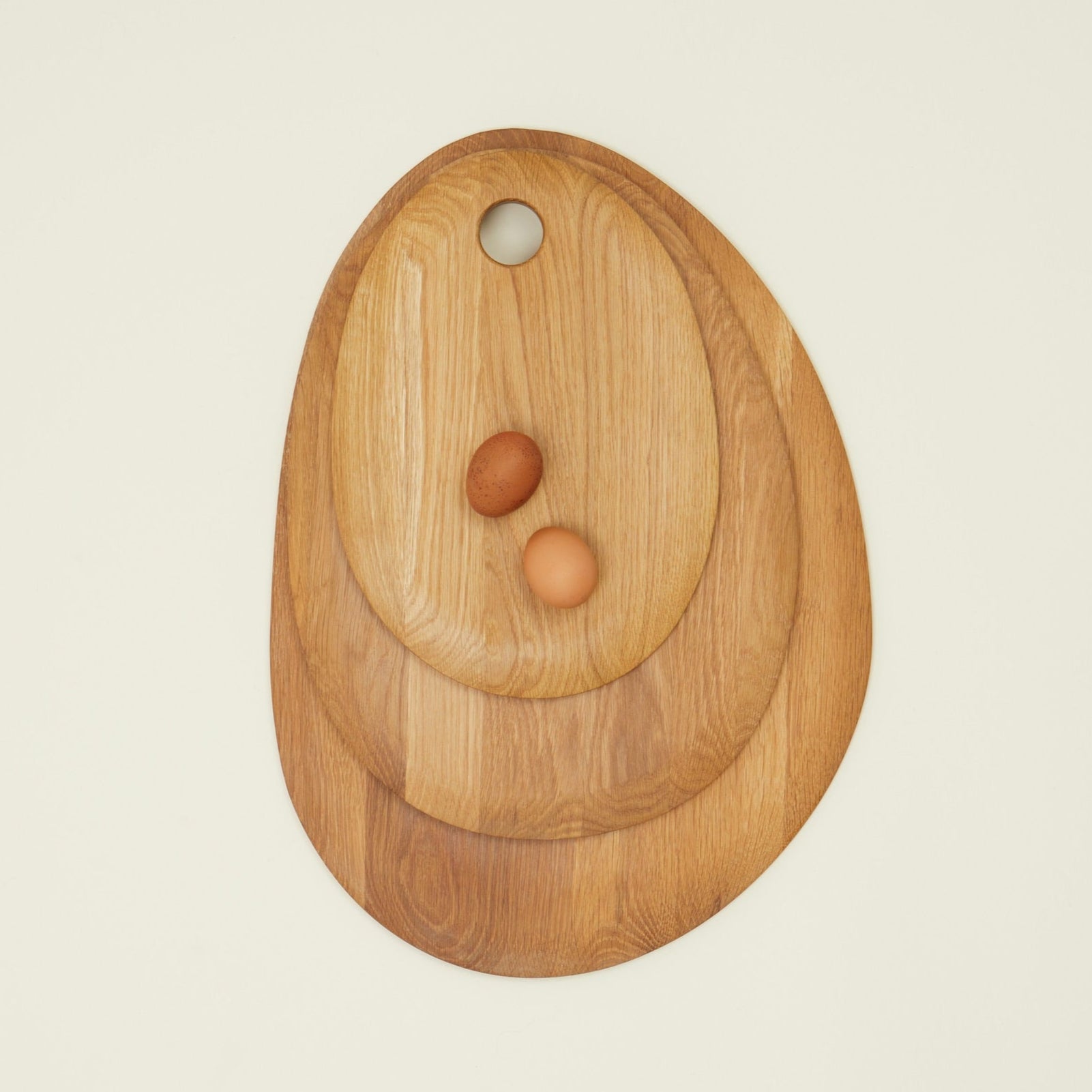 An oak wood cutting board with a circular shape and a handle in the center, featuring two eggs on the surface.
