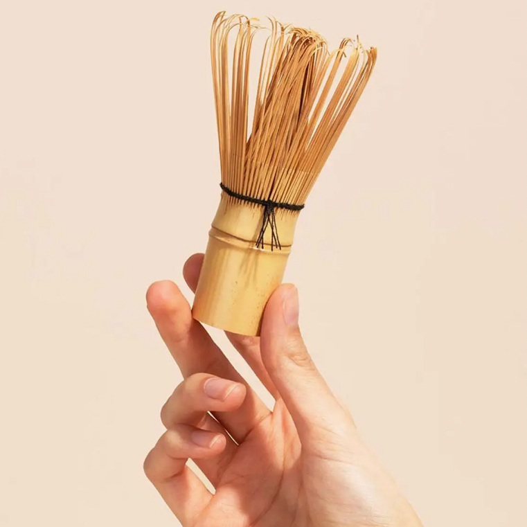 A hand holding a bamboo whisk, traditionally used for preparing matcha tea.
